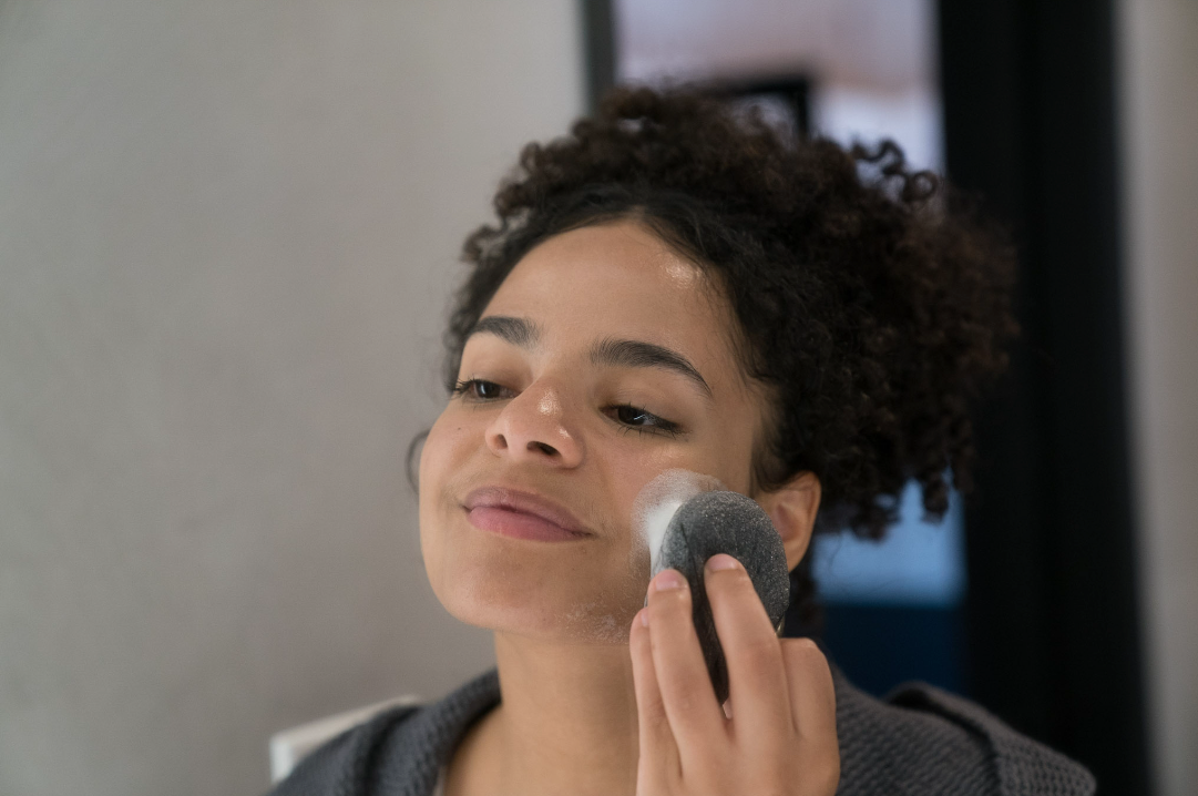 Woman washing her face with Face Foam and a konjac sponge.