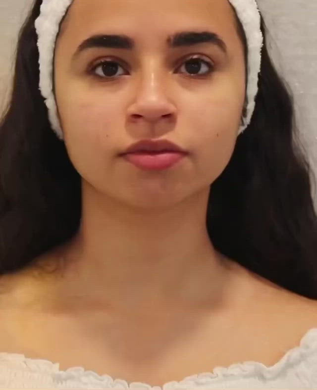 A close-up video of a woman applying a white bottle of natural retinol face moisturizer to her face and neck area.