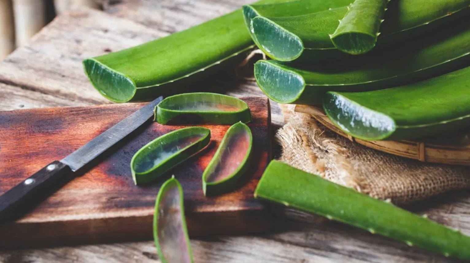 Slices of aloe vera on a wooden cutting board on a wooden table top.