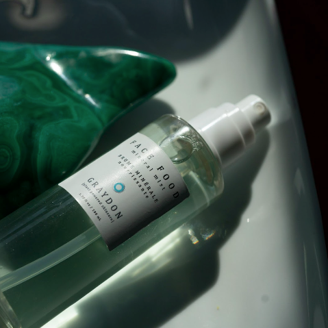 Bottle of Graydon Skincare Face Food Mineral Mist laying next to a beautiful green malachite stone.