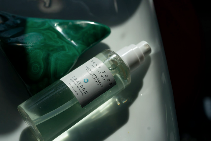 Bottle of Graydon Skincare Face Food Mineral Mist laying next to a beautiful green malachite stone.