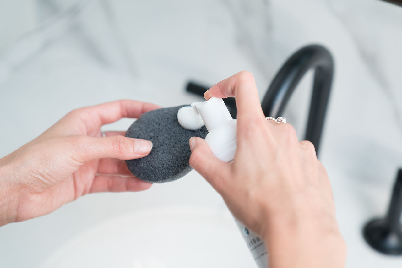 A fragrance-free foaming cleanser being dispensed on a bamboo charcoal konjac sponge. 
