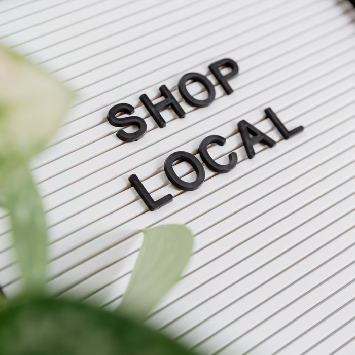 A whiteboard displays Shop Local in the center, as greenery peeks in from the left side of the frame.
