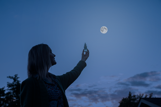 A shadow of a woman holding a bottle of Fullmoon Serum with a full moon in the night sky