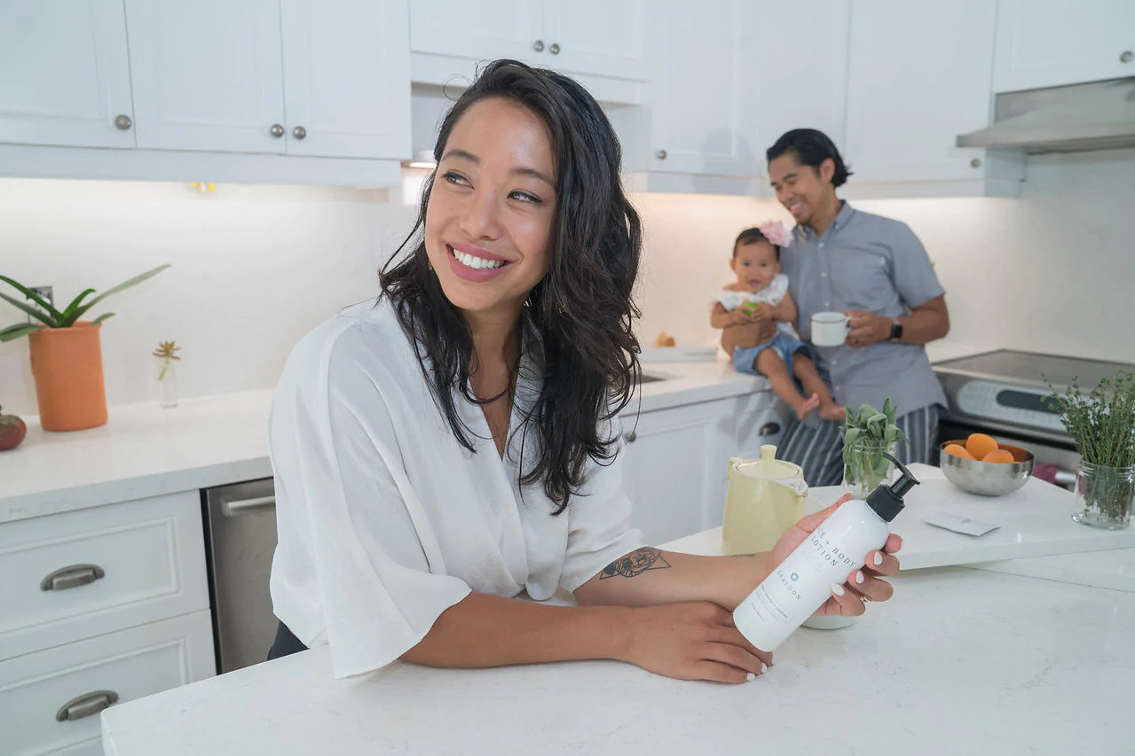woman in kitchen holding all over face and body lotion with husband and kid smiling in background