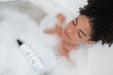 A woman taking a bath with a multipurpose body wash floating in the water.