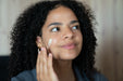A woman applying a white ceramide moisturizing face and eye cream to her face.